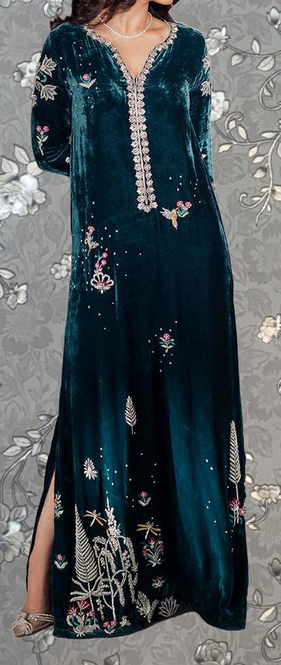 A woman wearing a long, green velvet dress with intricate embroidered designs on the front.