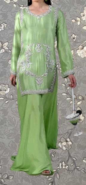 A woman wearing a long, green dress with intricate embroidery and holding a glass of wine.