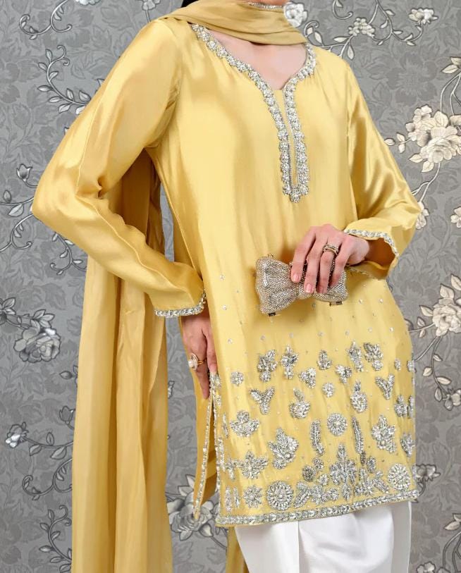 A person wearing a yellow dress with silver embroidery and holding a small clutch purse.