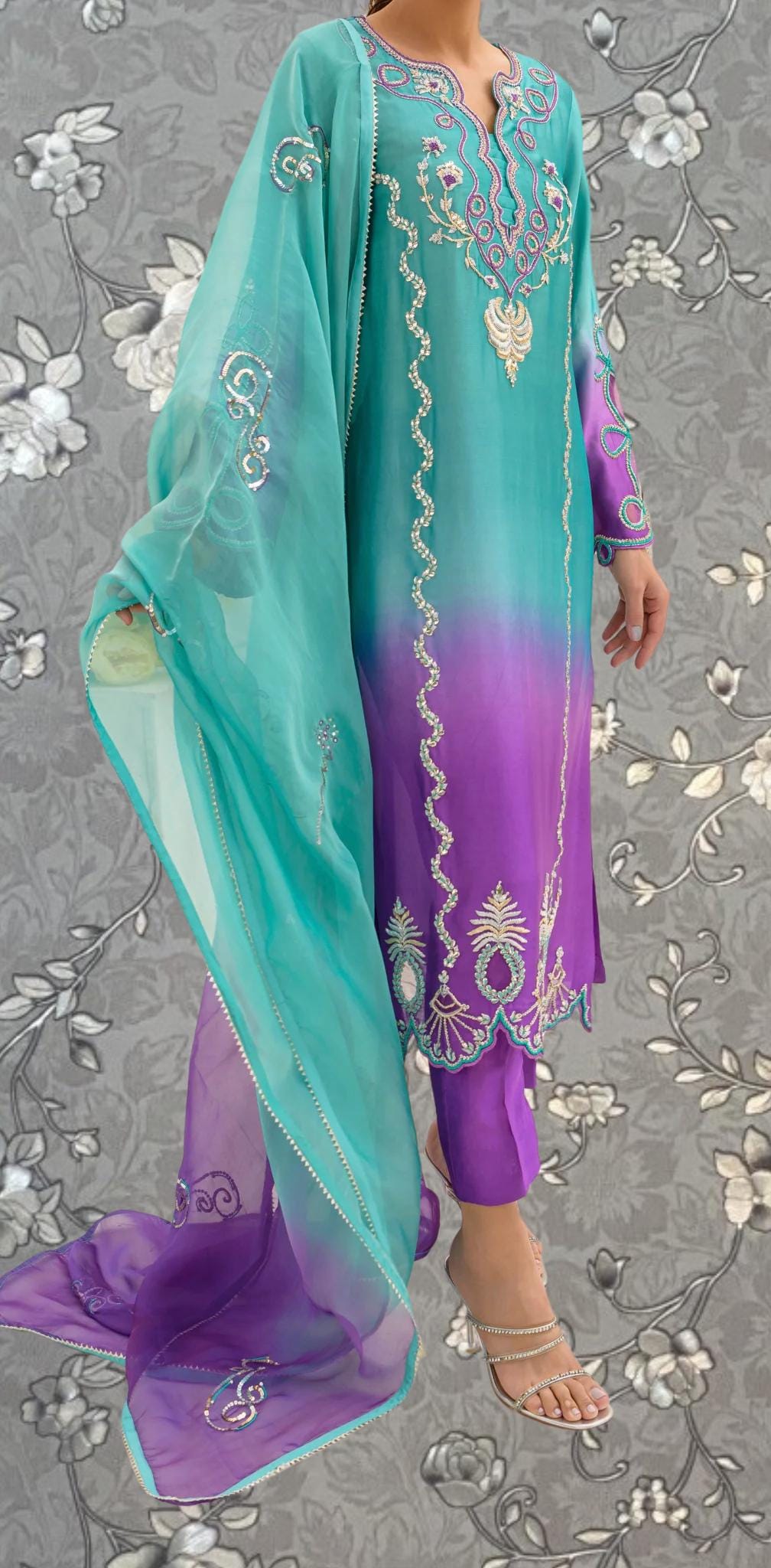 A person wearing a vibrant purple and teal dress with intricate embroidery and a matching shawl.