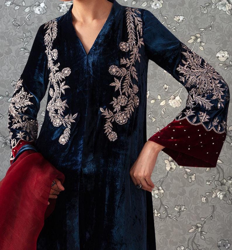 A person wearing a long, blue velvet dress with intricate embroidered designs on the sleeves and collar.