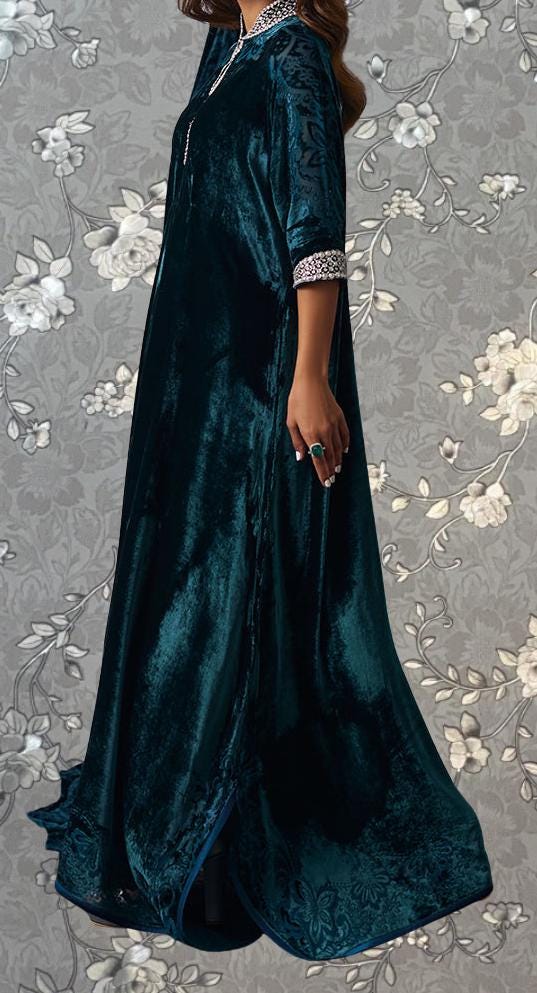 A woman wearing a long, dark blue velvet dress with a floral pattern on the background.