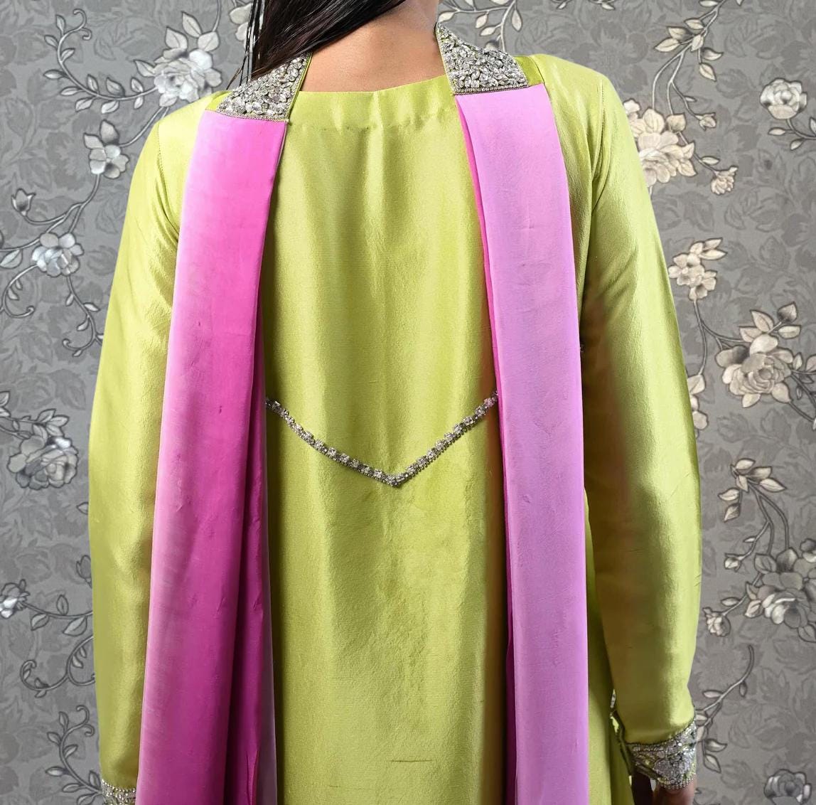 A close-up view of a person wearing a bright green dress with a pink sash, against a floral patterned background.