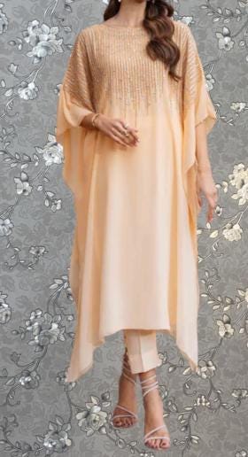 A woman wearing a peach-colored dress with a floral pattern, standing against a gray floral background.