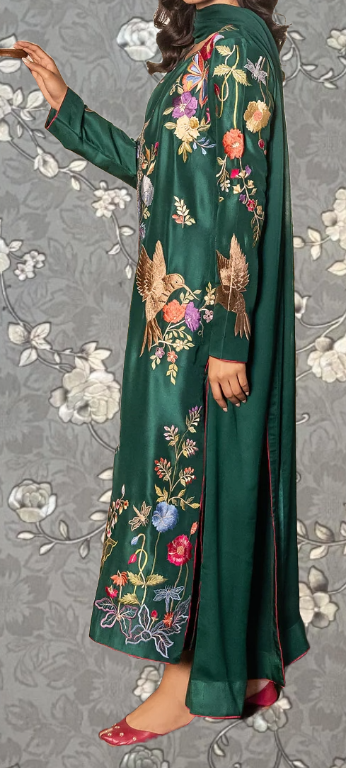 A person wearing a long green dress with intricate floral embroidery on the sleeves and hem.