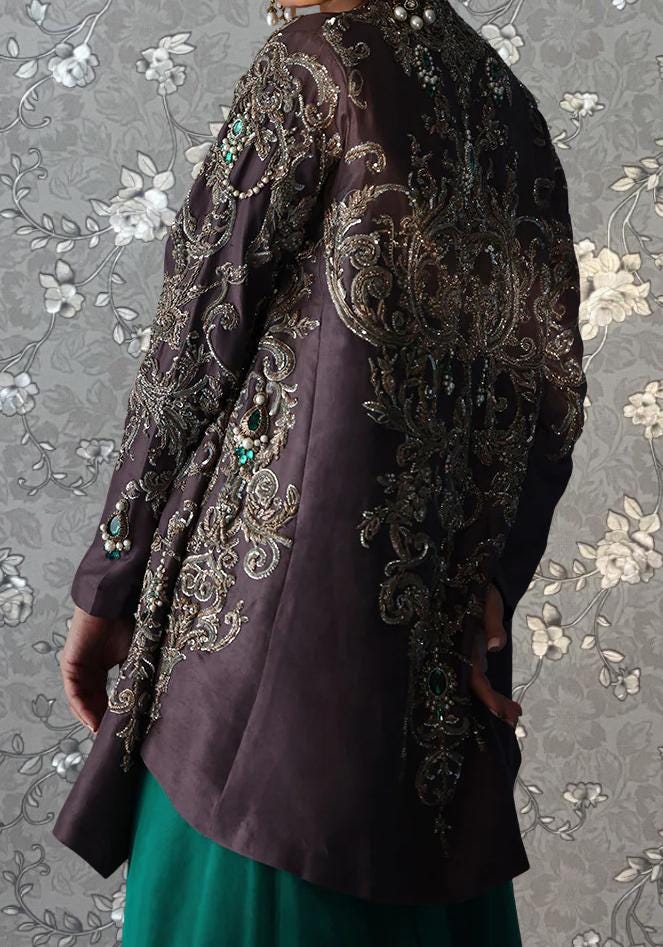 a person wearing an ornate, purple jacket with intricate embroidery and embellishments. The jacket appears to be a formal or evening garment, with the person standing against a patterned background.