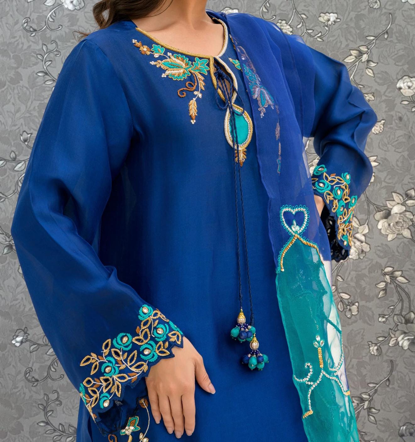 A close-up of a person wearing a blue dress with intricate embroidery and a matching blue shawl.