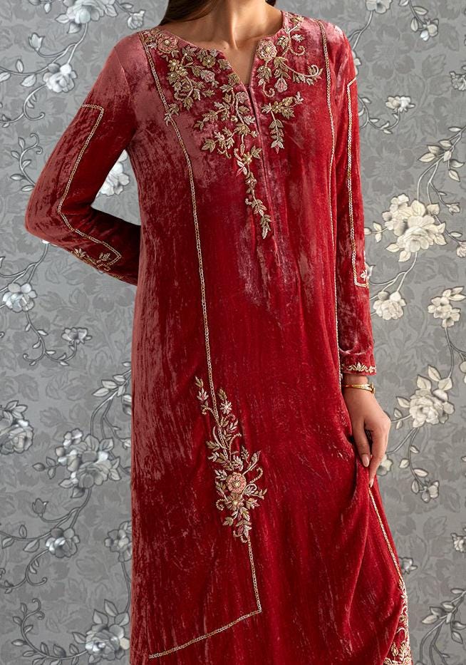A woman wearing a long, red velvet dress with intricate embroidered designs on the front.