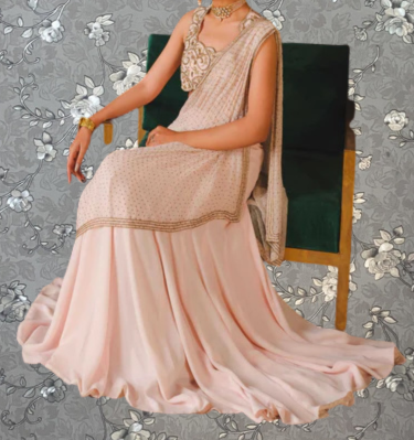A woman wearing a long, pink dress with a gold and beige patterned skirt is sitting on a green chair against a gray floral background.