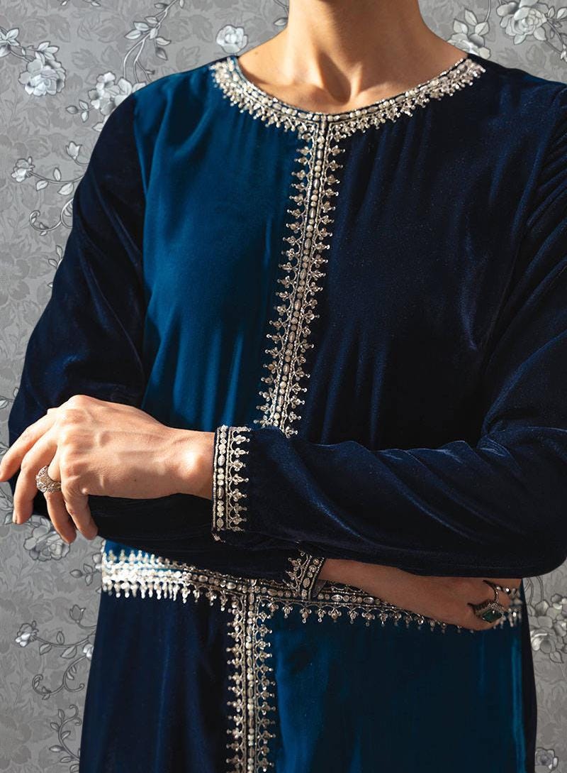 A person wearing a blue velvet dress with intricate silver embroidery on the neckline and sleeves.