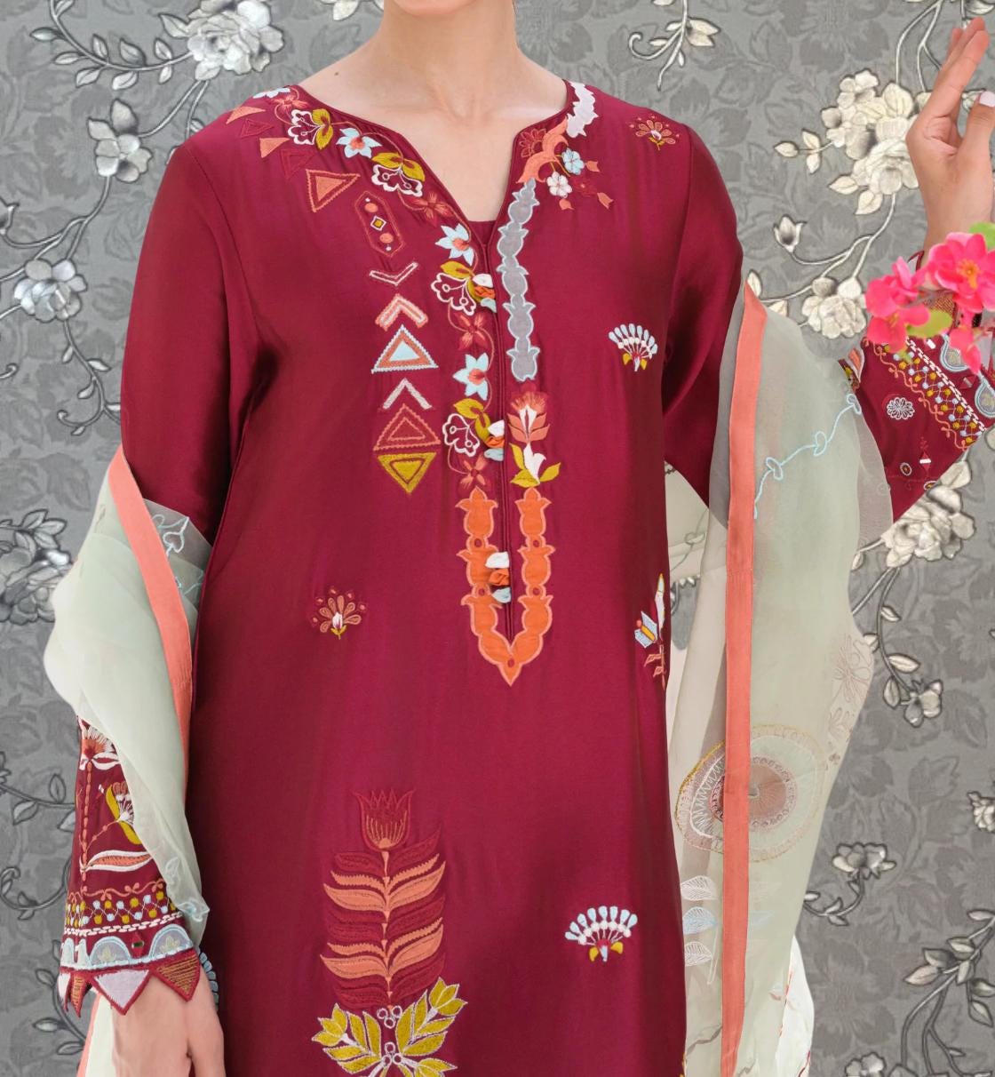 A close-up of a person wearing a red dress with intricate embroidered patterns and designs.