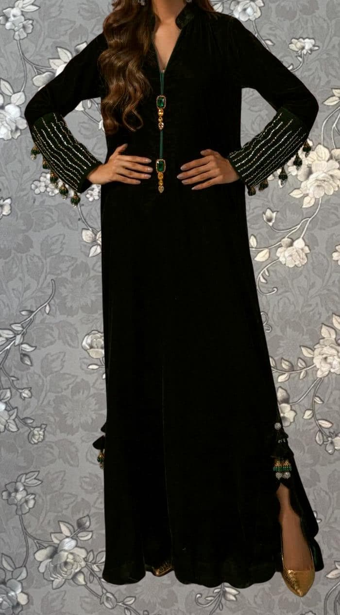 A woman wearing a long black dress with green accents and tassels on the sleeves.