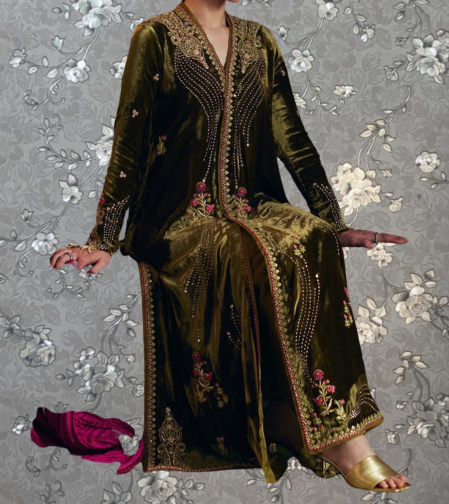 A woman wearing a long, ornate gold and black dress with intricate embroidery, sitting on a chair against a gray floral background.