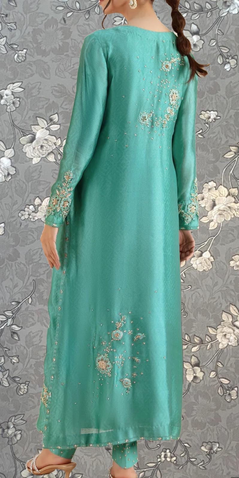 A woman wearing a long, mint green dress with intricate embroidered designs on the back.