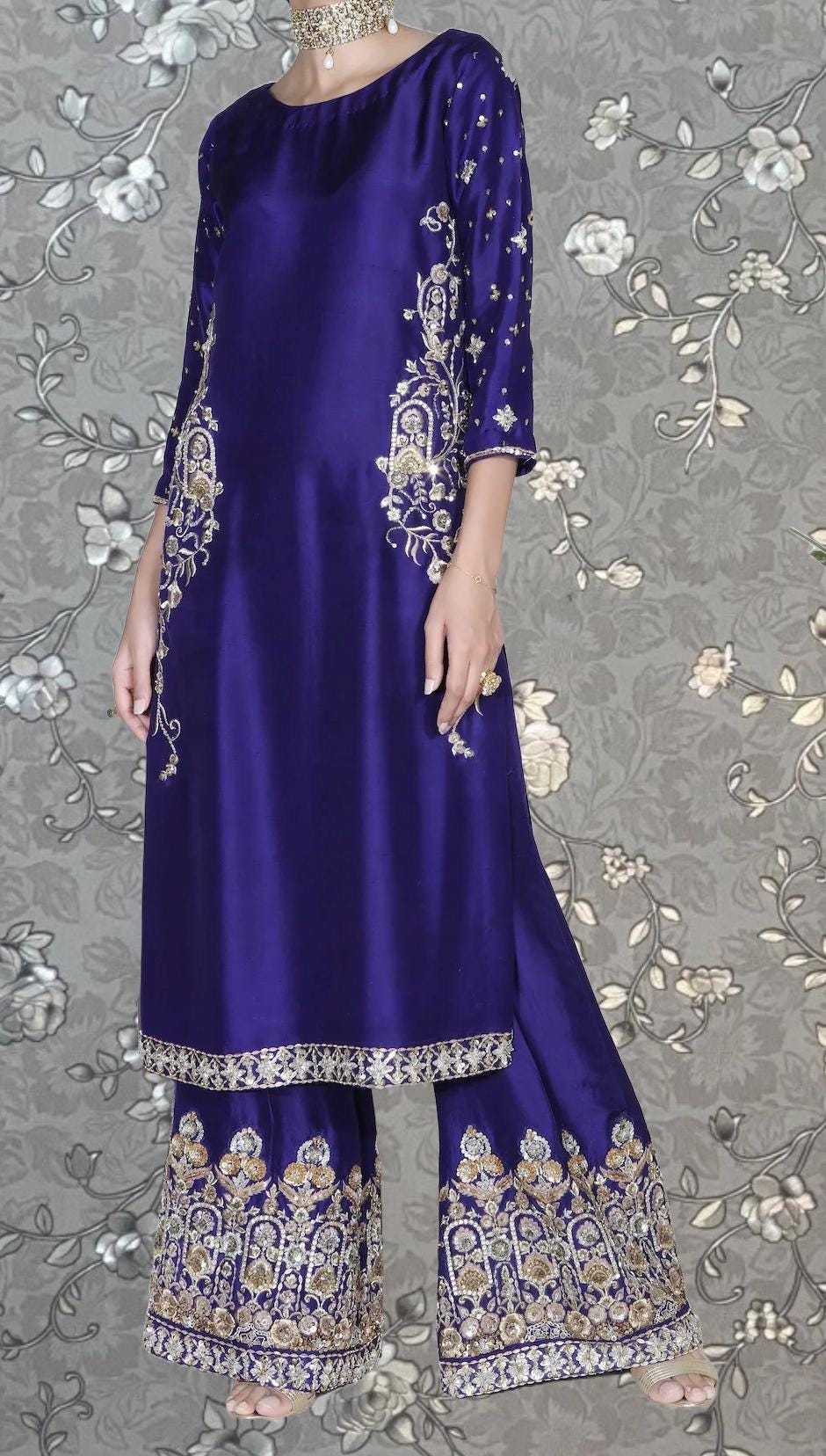 A woman wearing a long, purple dress with intricate gold embroidery on the sleeves and hem.