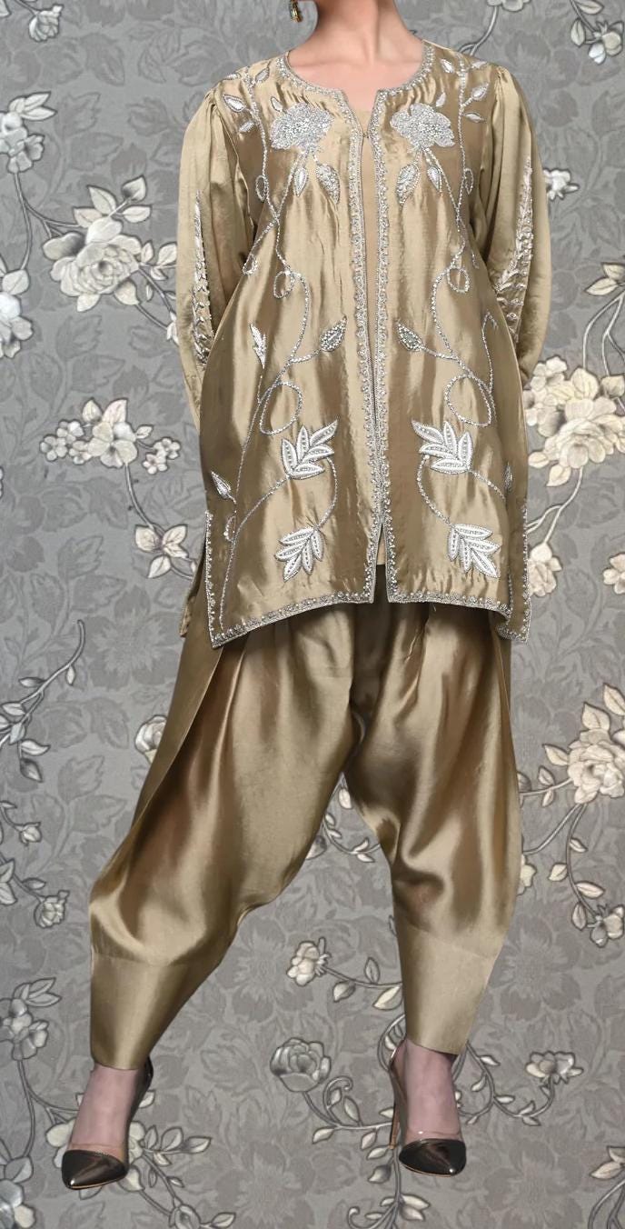 A woman wearing a gold and white patterned dress with a floral design, standing against a gray floral background.