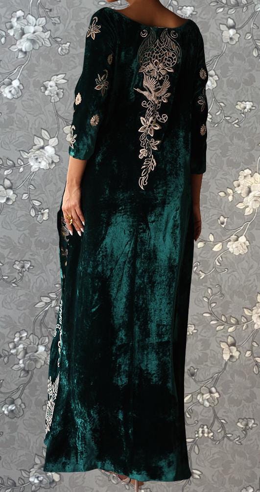 a person wearing a long, green velvet dress with intricate embroidered designs on the back.