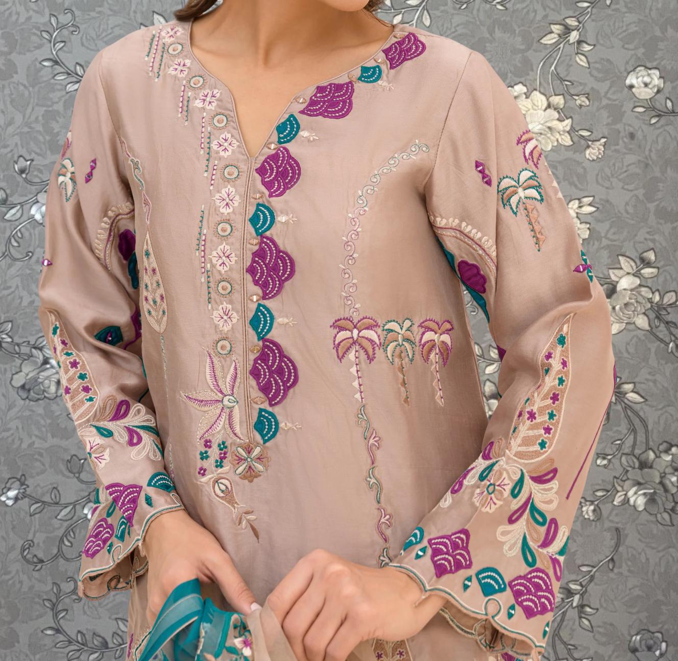 A close-up of a person wearing a beige dress with intricate embroidered patterns in shades of pink, blue, and green.