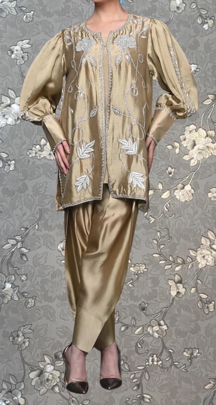 A gold-colored dress with puffed sleeves and floral embroidery, worn by a person standing against a gray floral background.