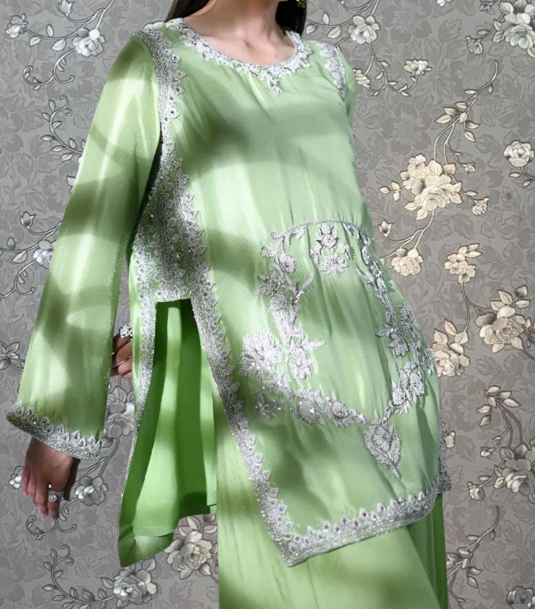 A woman wearing a green dress with intricate embroidery and floral patterns.