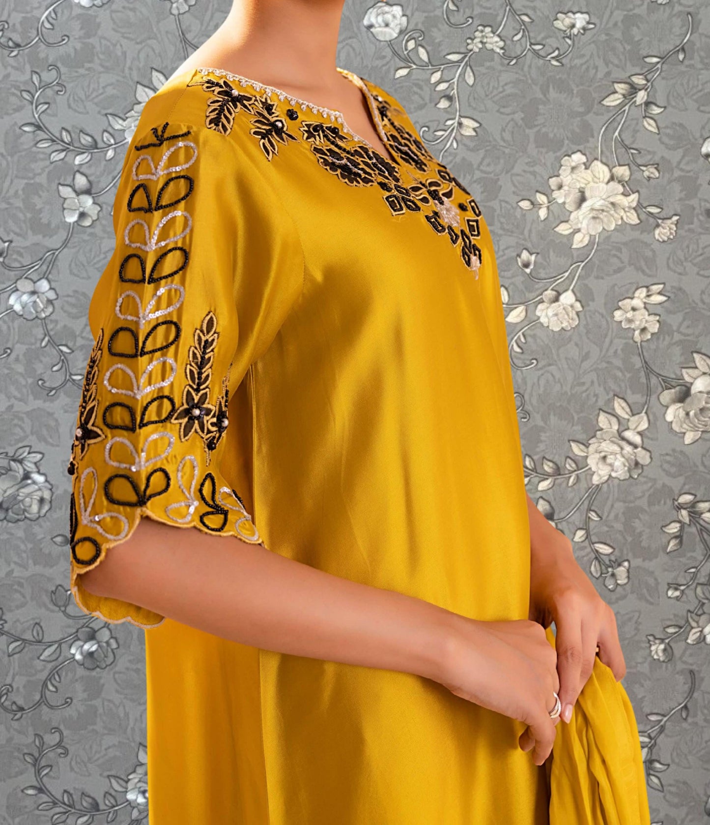 A woman wearing a yellow dress with black and white embroidered designs on the sleeves and neckline.