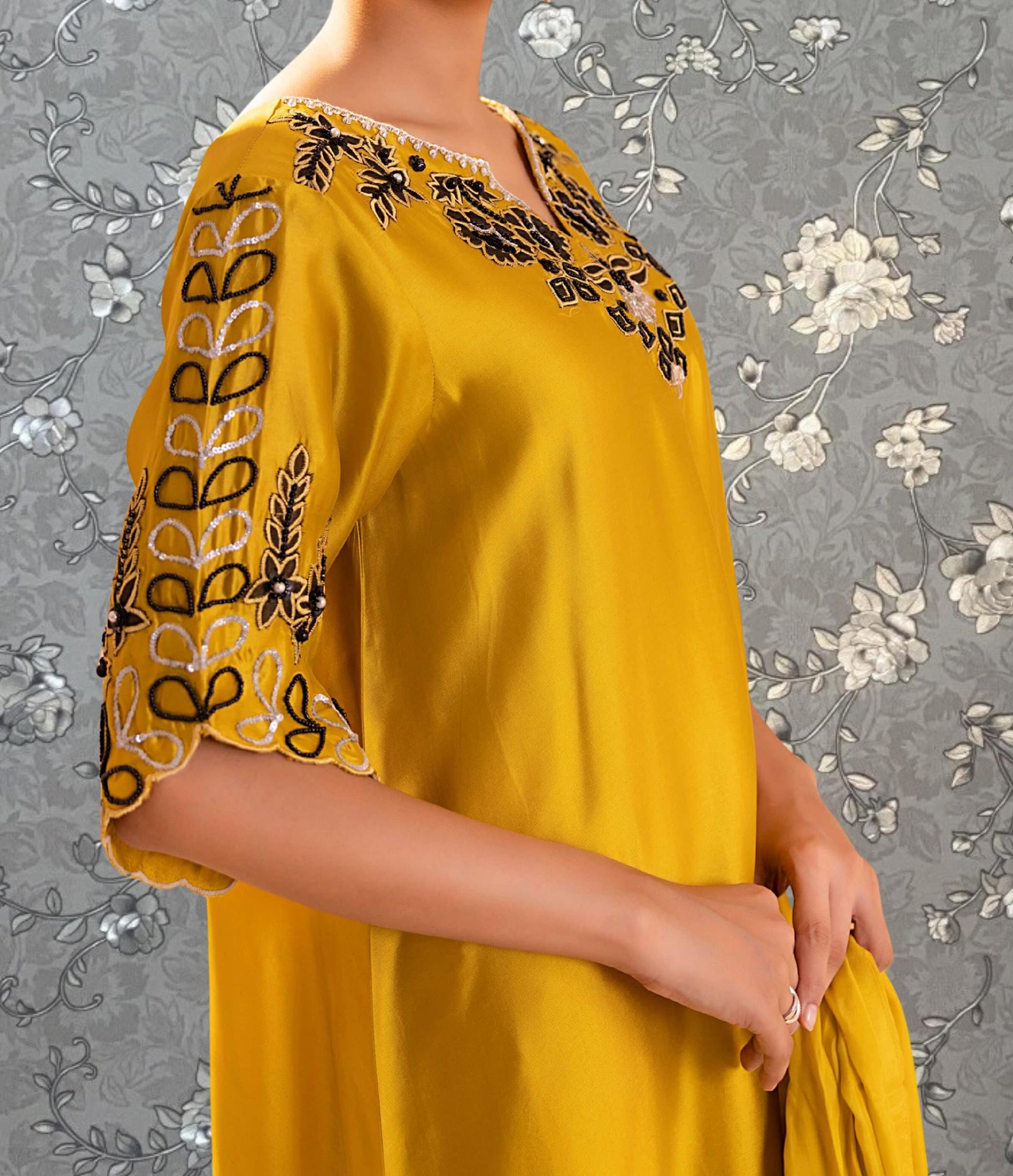 A woman wearing a yellow dress with black and white embroidered designs on the sleeves and neckline.
