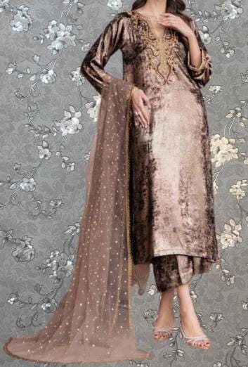 A woman wearing a long, brown dress with gold embroidery and a matching shawl stands against a gray floral background.