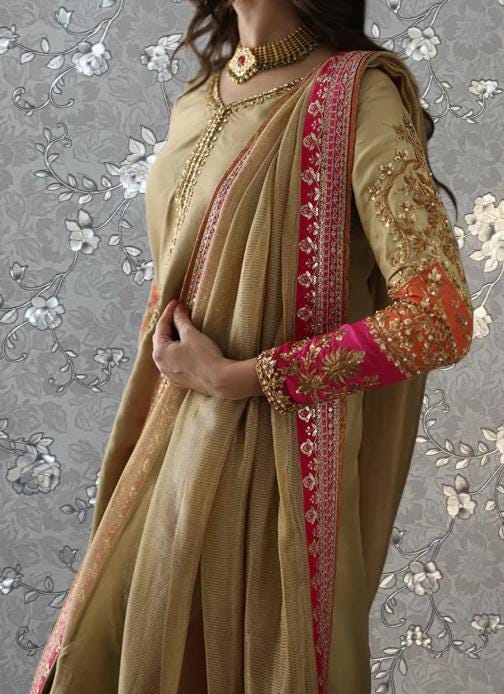 A woman wearing a gold and pink sari with intricate embroidery and jewelry poses against a floral background.