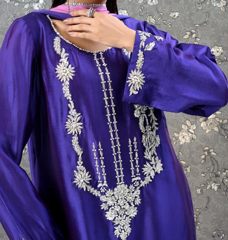 A close-up of a person wearing a long purple dress with intricate embroidered designs.