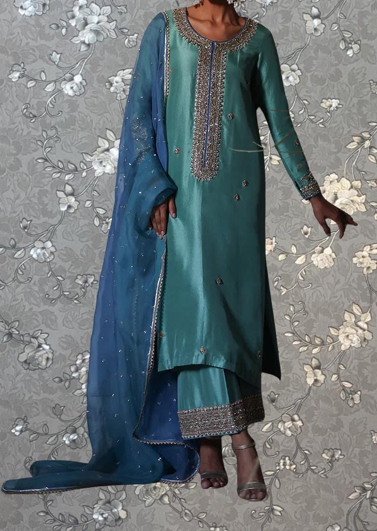 A woman wearing a long, green dress with intricate embroidery and a matching blue shawl.