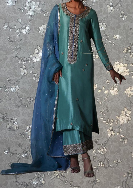 A woman wearing a long, green dress with intricate embroidery and a matching blue shawl.