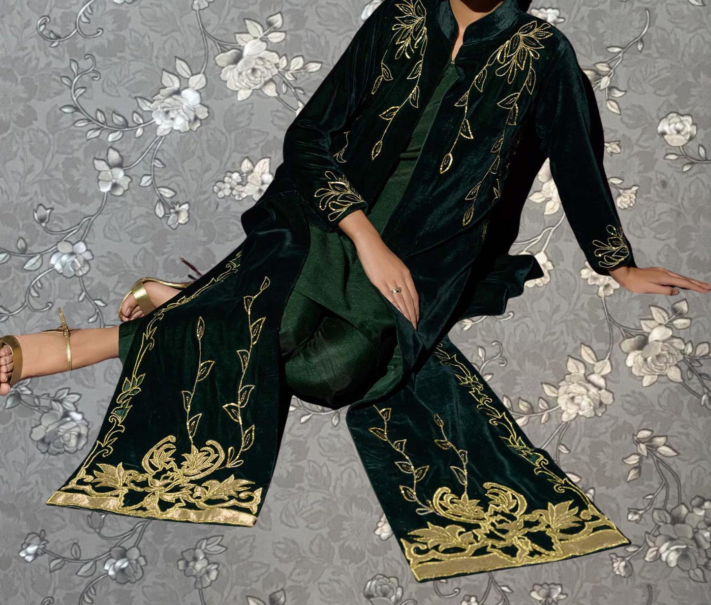 A person wearing a green and gold patterned dress is sitting on the floor against a gray floral background.