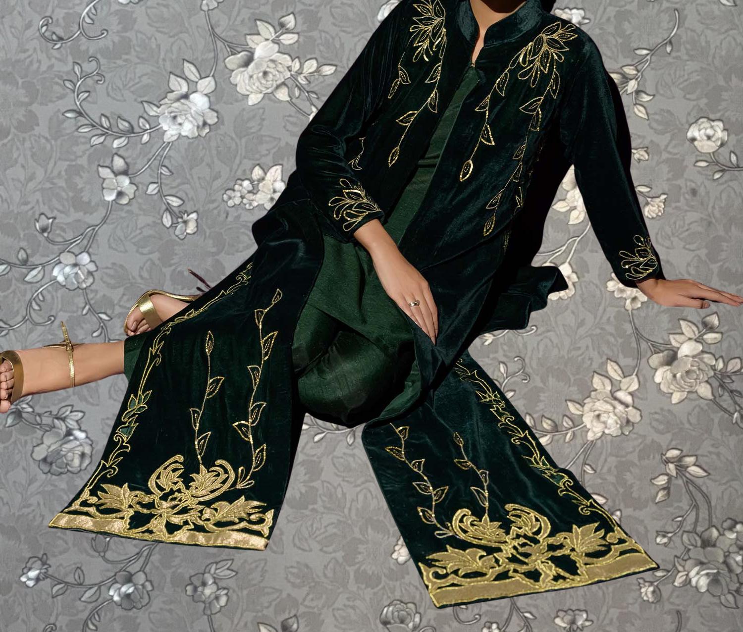 A person wearing a green and gold patterned dress is sitting on the floor against a gray floral background.