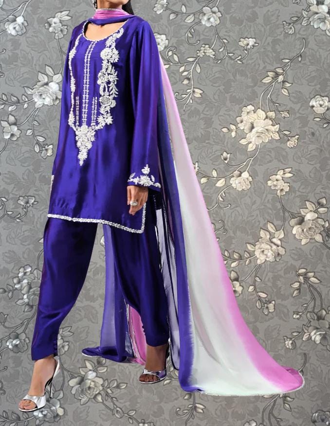 A woman wearing a purple and pink traditional Indian outfit with intricate embroidery and a long, flowing skirt.