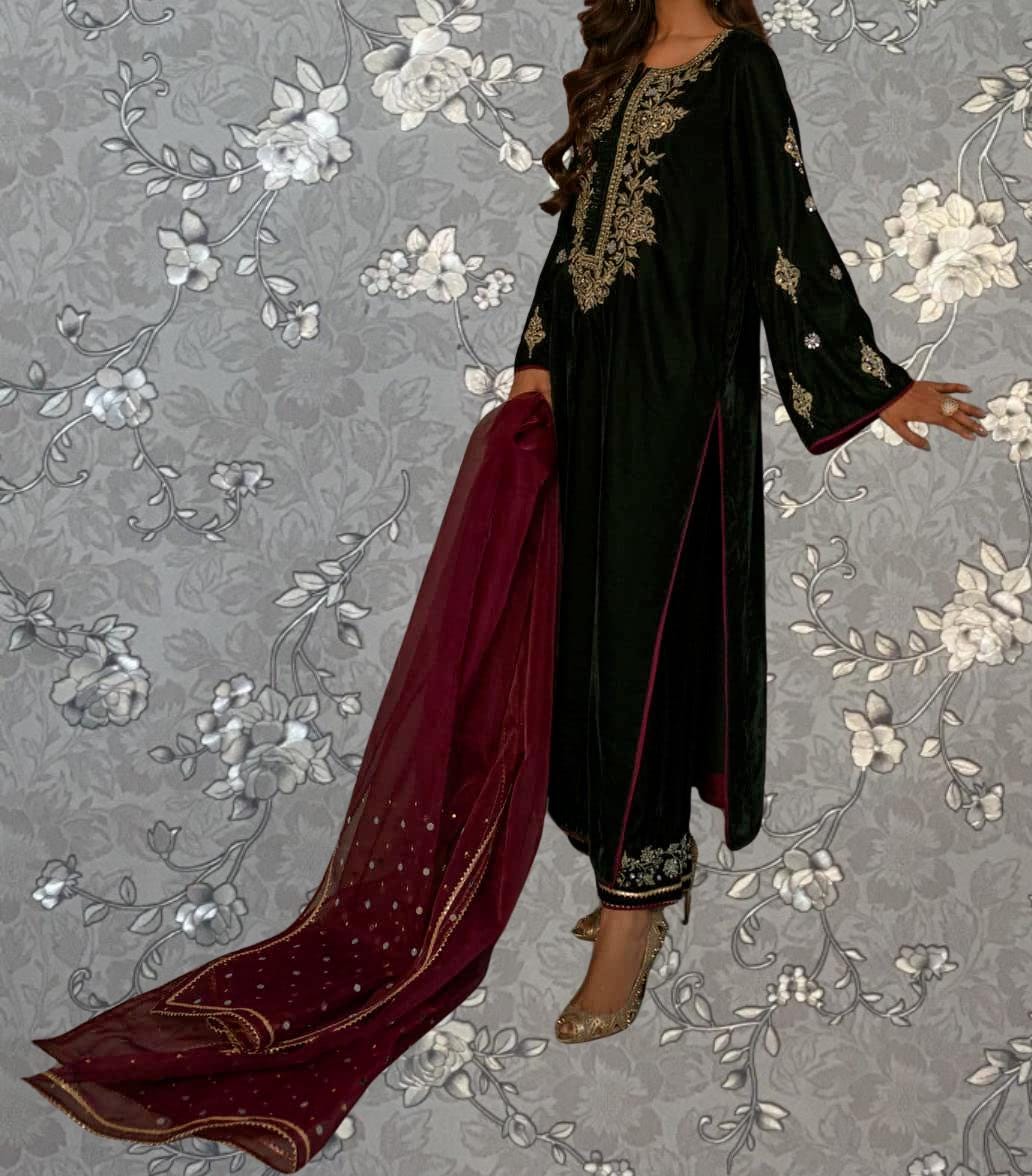 A woman wearing a black dress with gold embroidery and a red shawl stands against a gray floral background.