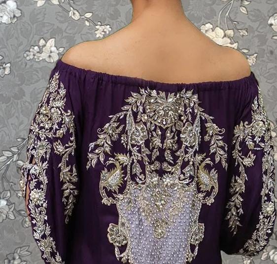 the back of a person wearing a purple off-the-shoulder dress with intricate embroidered designs.