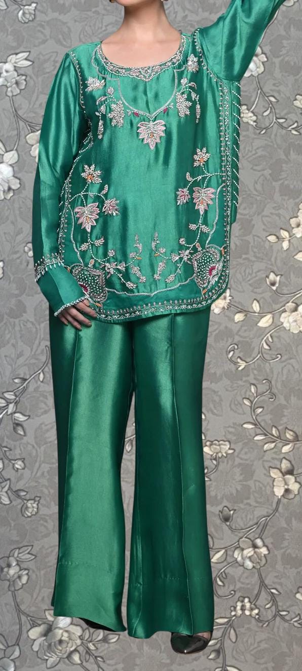 A person wearing a green satin top and matching pants with intricate floral embroidery.