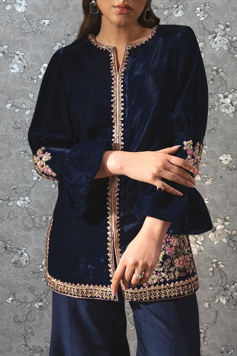 A woman wearing a navy blue velvet dress with gold embroidery and a floral pattern on the sleeves and hem.