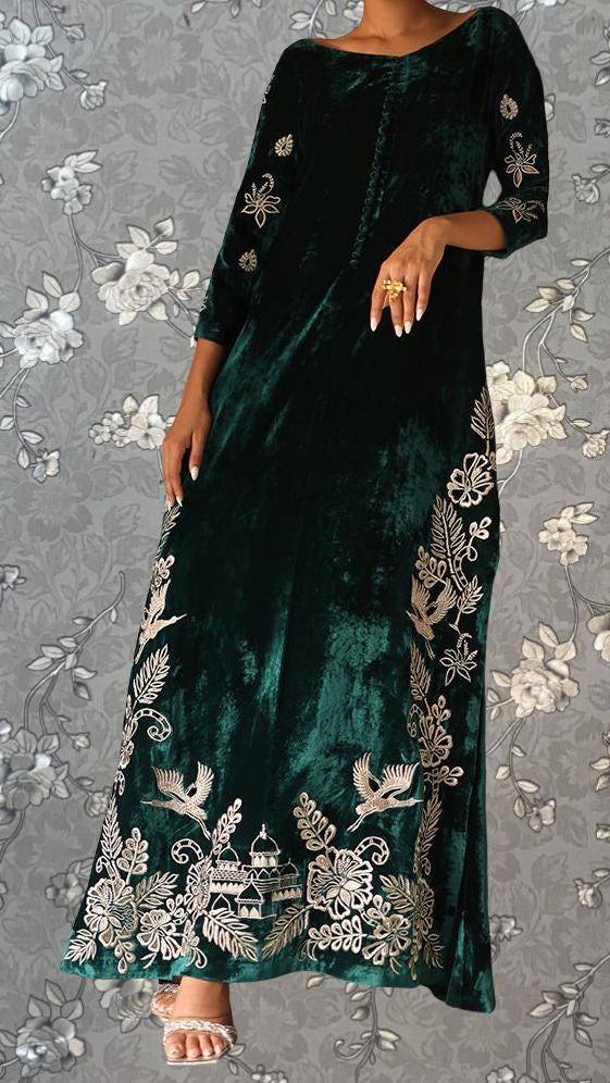 A woman wearing a long, green velvet dress with intricate gold embroidery on the sleeves and hem.