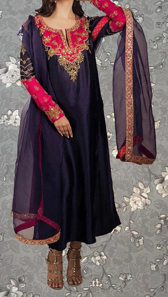 A woman wearing a long, dark purple dress with red and gold embroidered details, including a matching shawl. She is posing with one hand on her hip and the other on her thigh.