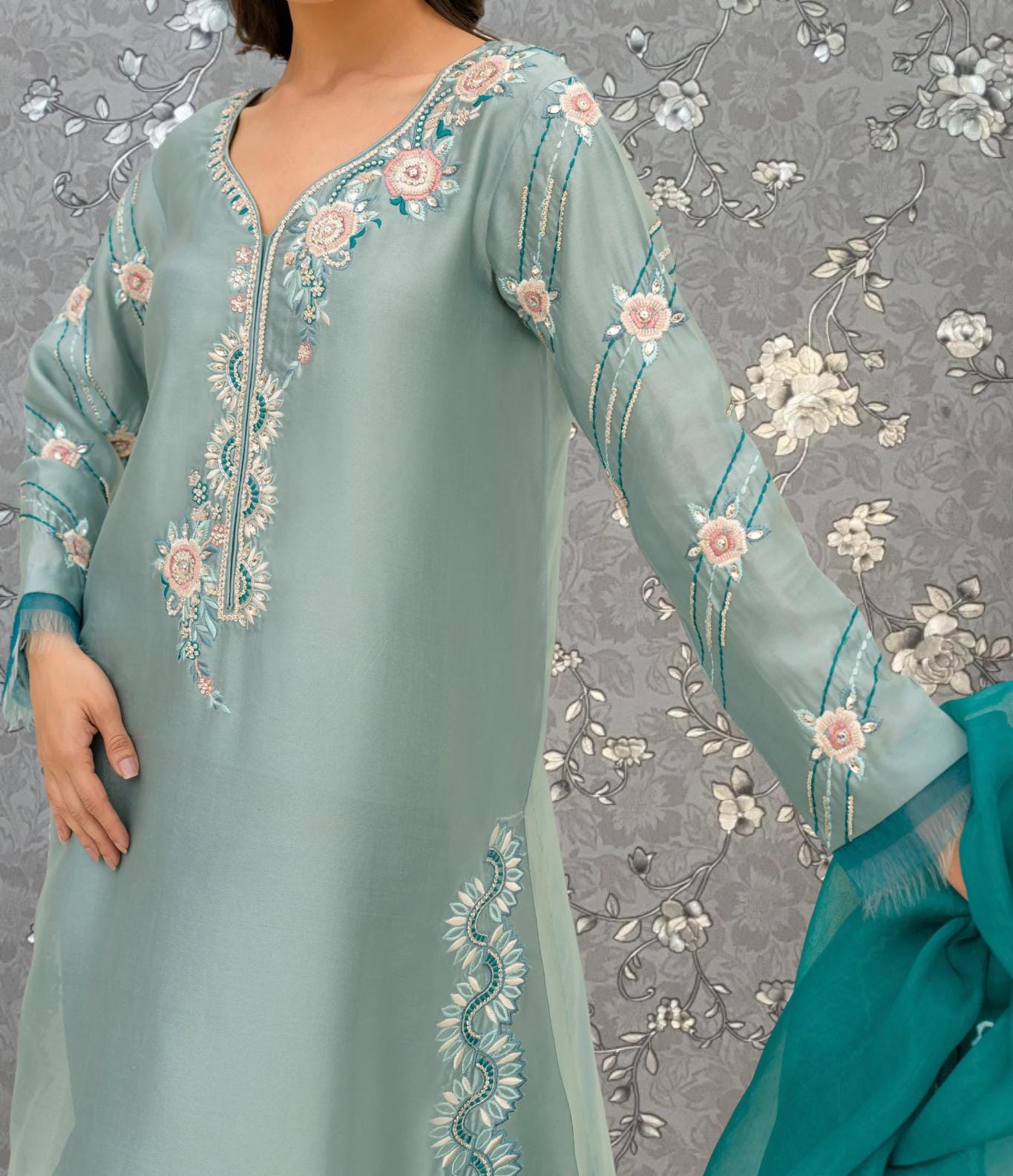A woman wearing a light blue dress with intricate floral embroidery on the sleeves and collar.