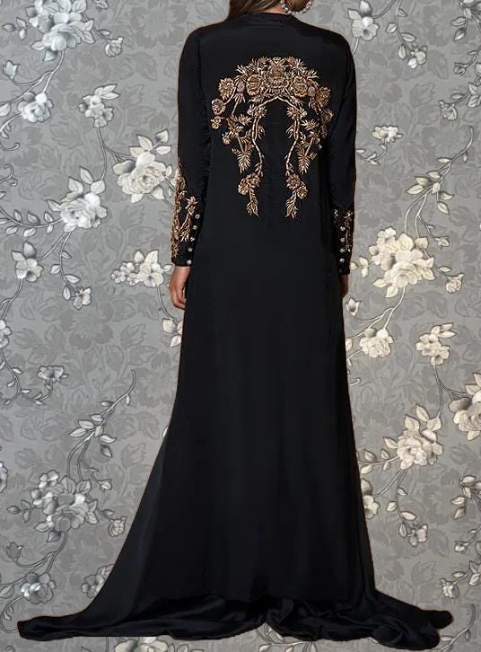 A person wearing a long black dress with gold embroidered designs on the back.