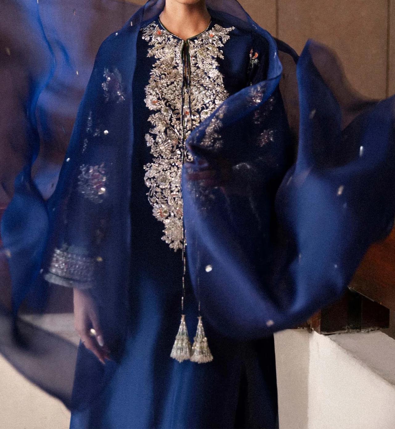 A person wearing a blue dress with intricate embroidery and a matching blue shawl.