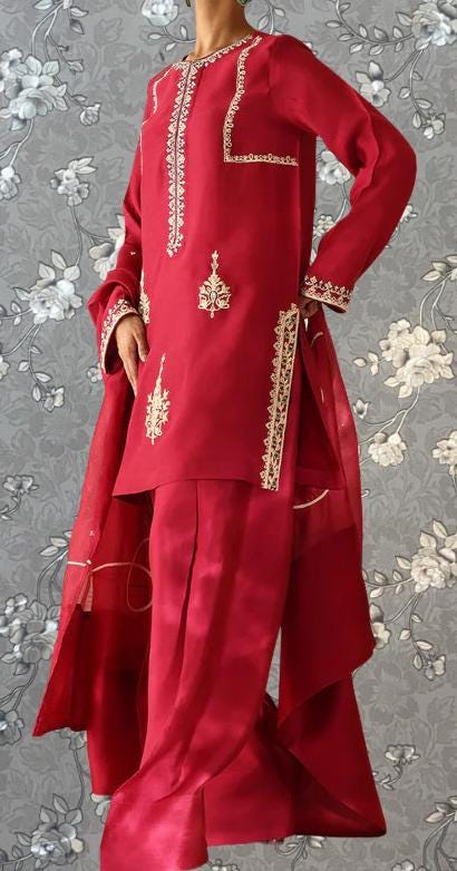 A red and gold dress with intricate embroidery and patterns, displayed against a gray floral background.