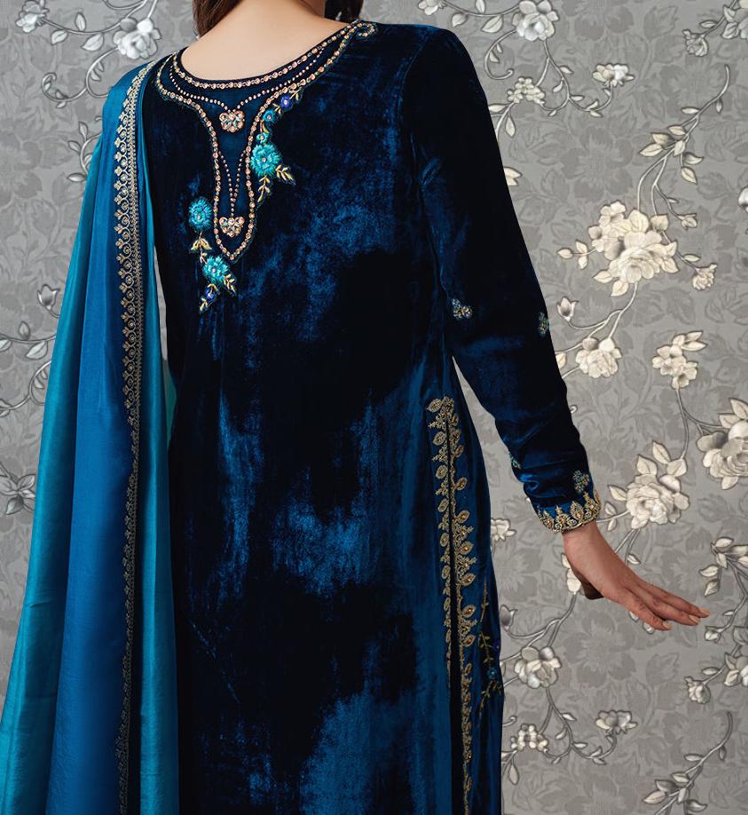 A close-up view of a woman wearing a blue velvet dress with intricate embroidery and gold accents.