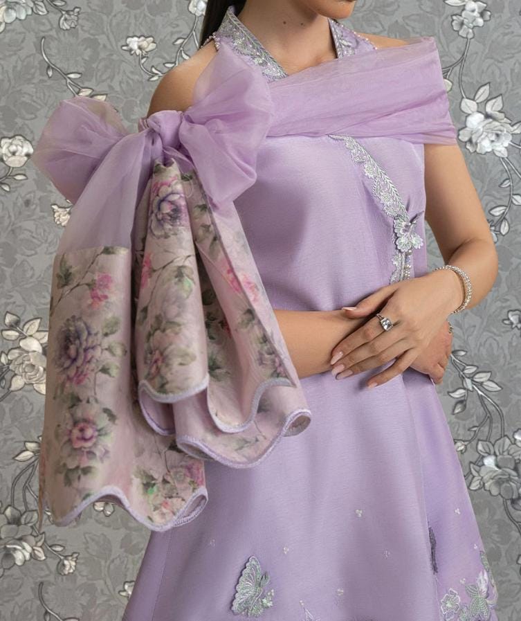 A woman wearing a lavender dress with a floral pattern and a large bow on the shoulder.