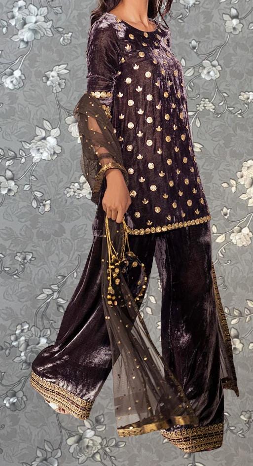 A woman wearing a purple velvet dress with gold polka dots and gold accents, holding a gold and black accessory.