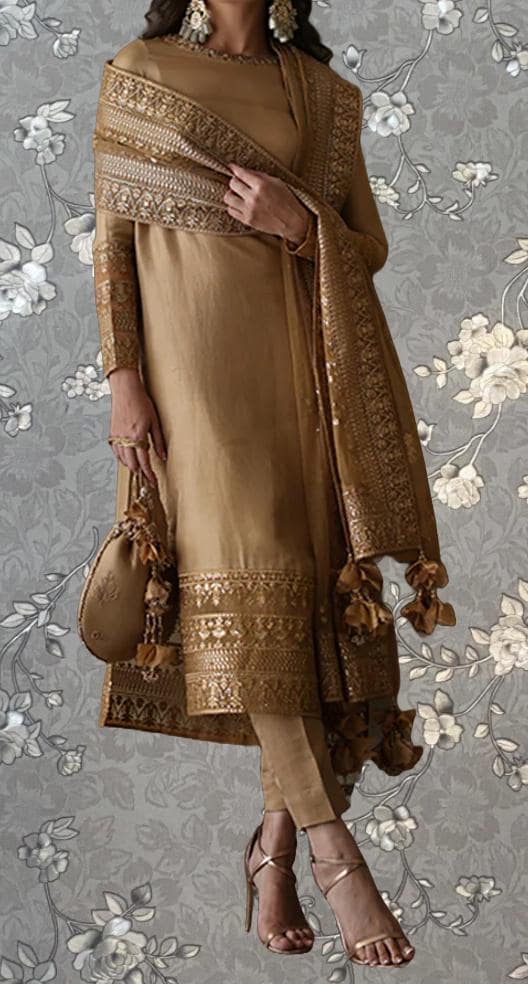 A woman wearing a gold and beige dress with a matching shawl, standing against a gray floral background.
