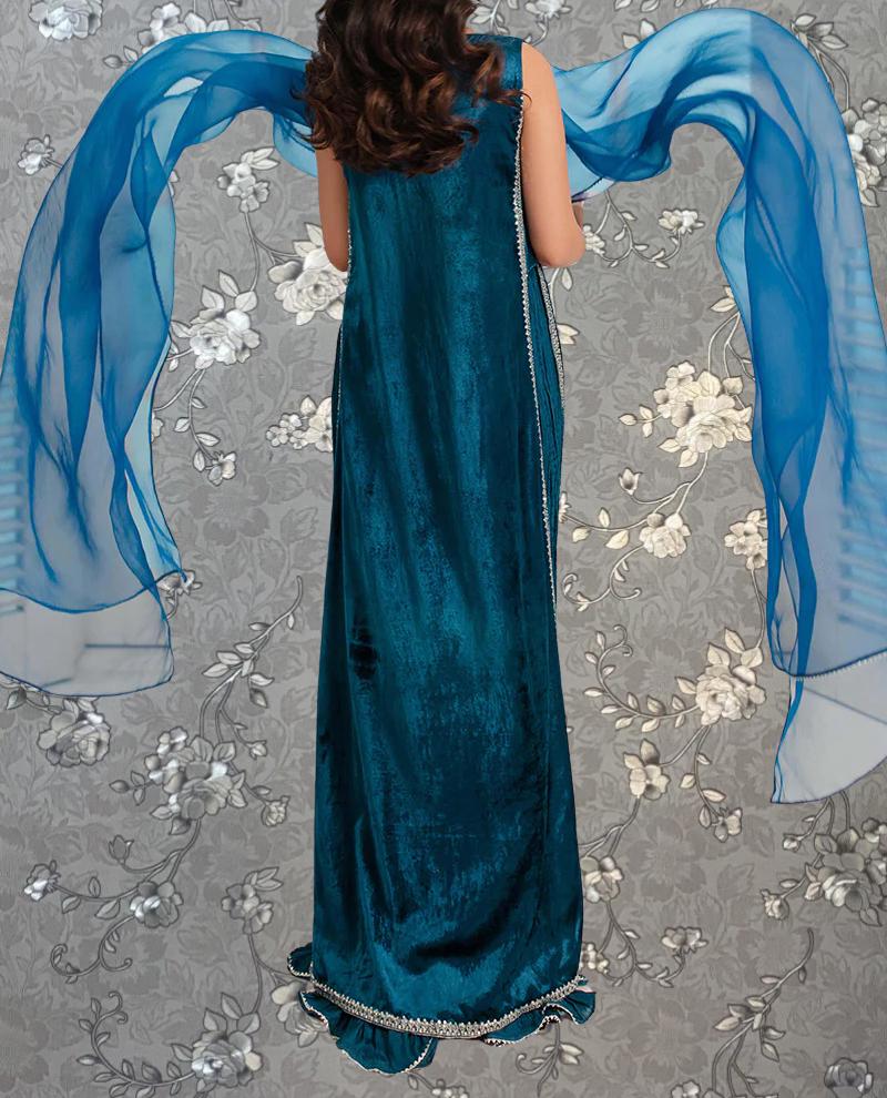 A woman wearing a long, blue dress with a flowing skirt and a blue scarf is standing against a gray floral background.