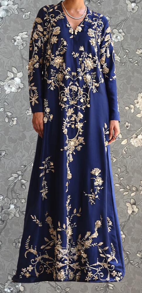 A woman wearing a long, blue dress with intricate gold embroidery.
